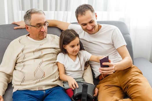 grandfather and granddaughter, father with smartphone at home.