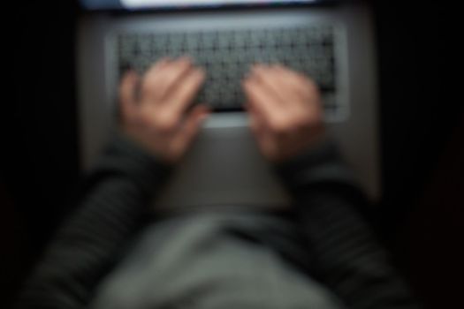 Overhead hacker in the hood working with laptop and mobile phone typing text in the darkroom. Russian hacker hacking the server in the dark. A hacker girl sitting in the dark with her laptop. Blurred image