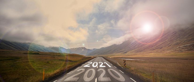 The word 2021 written on highway road in the middle of empty asphalt road at golden sunset and beautiful blue sky. High-quality photo