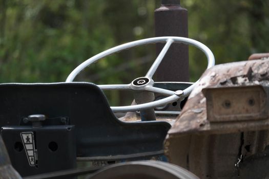 The steering wheel of an old tractor seen from close up. Side view with steering wheel, control panel, gearbox, handbrake and adjustable seats.