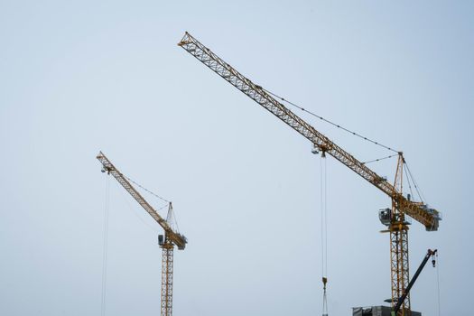 Tower cranes working on a construction site lifts a load at high-rise building in summer day. A large construction site with busy cranes.