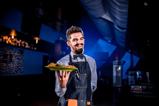 Stylish restaurant employee offers visitors plate with prepared dish on a black background.