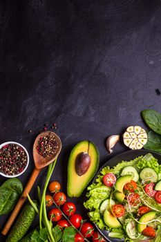 Ingredients for making salad on rustic black chalk board background. Vegetable salad in bowl, avocado, tomato, cucumber, spinach. Healthy, clean eating concept. Vegan or gluten free diet. Copy space