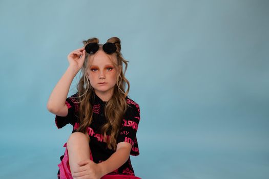 fashion teenager portrait. tween school girl with orange makeup wearing pink stylish cool clothes on blue background.