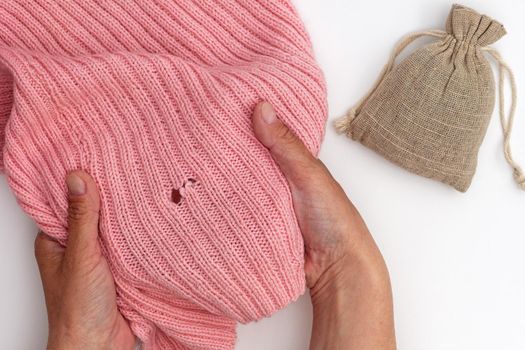 Top view of cropped woman hands holding pink wool fabric with hole made by moth and bag with dry herb on white background