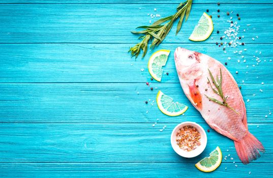 Fresh fish tilapia ready to cook. Raw fish with herbs, lemon, salt, pepper on wooden rustic background. Ingredients for cooking or making healthy dinner. Fish background. Space for text. Diet/healthy