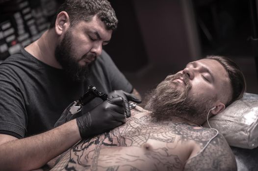 Master tattooist create tattoo in tattoo studio.