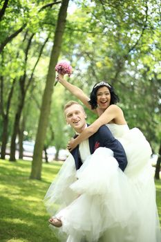 groom carries his bride on the back in the Park on a Sunny day