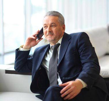 Smiling businessman sitting and talking on the phone at office