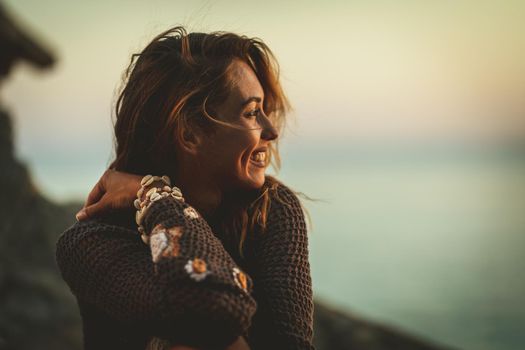 A beautiful young pensive woman is thinking and relaxing on the beach at the sunset. 