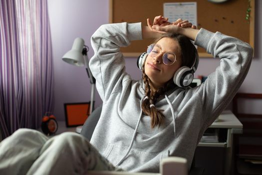 Hands above your head and eyes closed. Complete relaxation while listening to music. Young girl with pigtails and glasses is listening to music.