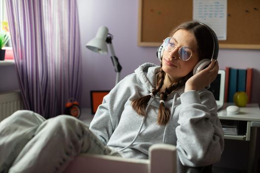 A teenage girl muses while listening to her favorite music. A young girl looks into the distance with headphones on her ears.