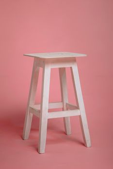 An old chair, a wooden stool on a pink studio background.
