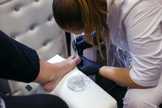 A cosmetologist who performs a nail procedure on a client