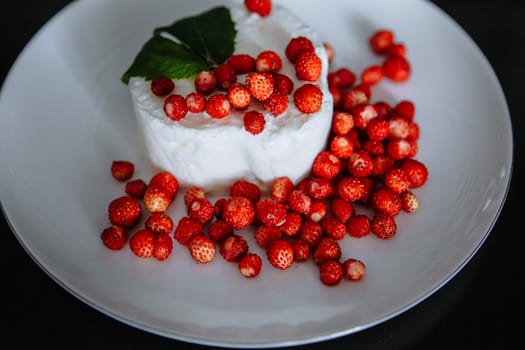 Lots of red strawberries laid out on a white plate with ice cream. Top with a mint leaf