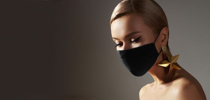 Beautiful woman with a black medicine mask on face. Fashion eye make-up, celebrate style, gold jewelry. Beauty with protection hygiene in viral covid-19 pandemic. Party christmas stylish