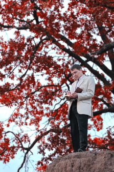 A man with a book in his hands stands against the background of a tree