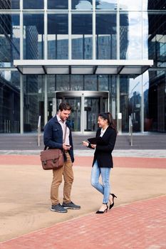 caucasian man and asiatic woman talking about business in front of the entrance to an office building, concept of coworkers and lifestyle, copy space for text