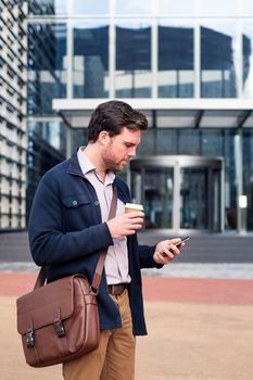 caucasian man consulting his phone at the entrance of the office building, concept of business and communication, copy space for text