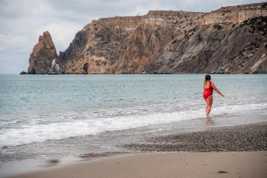 Woman in a bathing suit at the sea. A fat young woman in a red swimsuit enters the water during the surf.