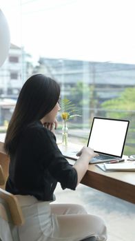 Back view of young female freelancer working online with computer laptop.