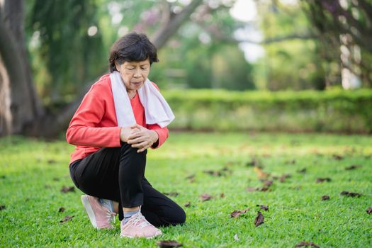 Senior asian woman with knee ankle pain while running in park. Senior asian woman sitting on the ground and holding painful knee.