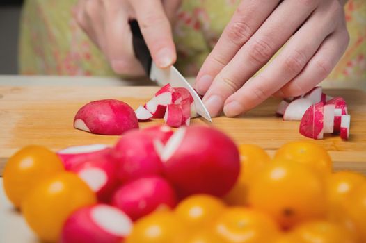 The fingers of a young woman cooking in the kitchen are cutting vegetables. Sliced radishes and tomatoes, close-up