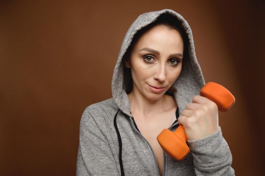 woman trainer in a hood with dumbbells in her hands. studio portrait.