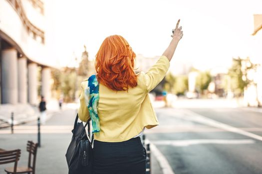 Rear view of a businesswoman who is standing by the street and calling for taxi.