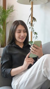 Casual millennial woman using mobile phone, checking social media, shopping online on sofa.