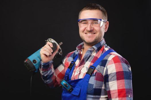 Portrait of a caucasian male repairman in a work uniform with an electric jigsaw around his neck. Studio portrait of an artisan businessman.