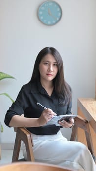 Portrait of young female manager sitting at modern workplace and looking confidently at camera.