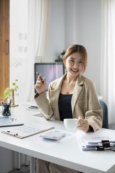 Confident female employee hand holding coffee cup and smiling to camera while sitting at her office desk.