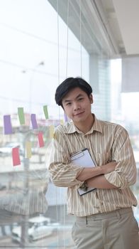 Thoughtful young businessman standing near the window in office building and smiling to camera.