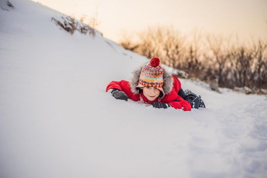 Boy in red fashion clothes playing outdoors. Active leisure with children in winter on cold days. Boy having fun with first snow. Happy little kid is playing in snow, good winter weather.