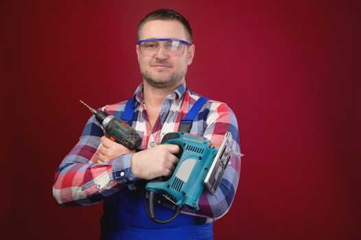 Portrait of a caucasian male repairman in a work uniform with an electric jigsaw around his neck. Studio portrait of an artisan businessman.