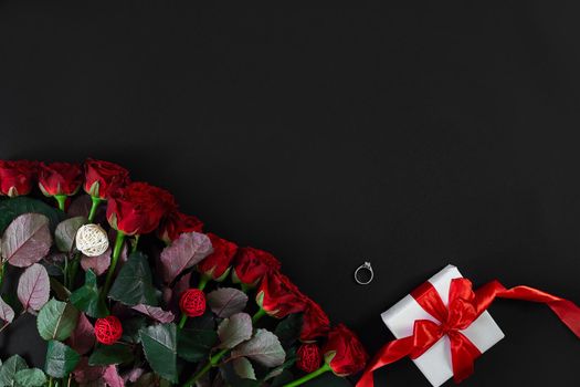 Red roses, ring and gift box on black background. Top view. Flat lay. Copy space. Still life