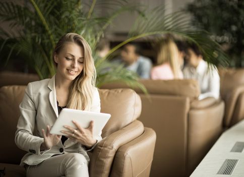 Successful business woman with a digital tablet sitting on the couch in the lobby of a modern office