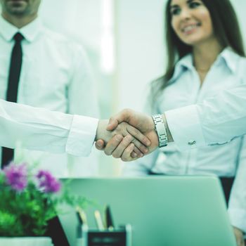 in the foreground - handshake of business partners on background of office workers.the photo has a empty space for your text