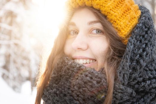 portrait of a smiling young caucasian woman in a bright woolen hat and scarf, against the backdrop of a snowy forest