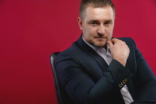 Portrait of a handsome man in an elegant suit on a red background. Studio shot looking thoughtfully into the camera