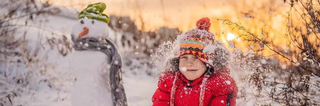 Cute boy in red winter clothes builds a snowman. Winter Fun Outdoor Concept. BANNER, LONG FORMAT