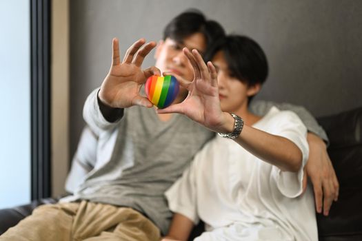 Happy young gay couple embracing and holding rainbow heart shape. LGBT, pride, relationships and equality concept.