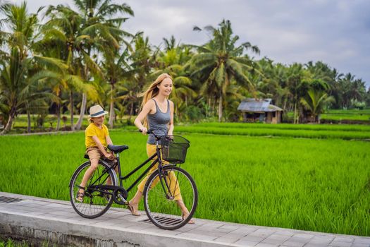 Mother and son ride a bicycle on a rice field in Ubud, Bali. Travel to Bali with kids concept.