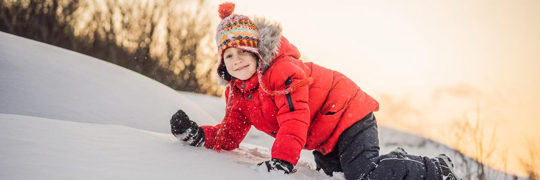 Boy in red fashion clothes playing outdoors. Active leisure with children in winter on cold days. Boy having fun with first snow. Happy little kid is playing in snow, good winter weather. BANNER, LONG FORMAT