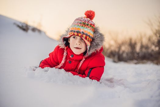 Boy in red fashion clothes playing outdoors. Active leisure with children in winter on cold days. Boy having fun with first snow. Happy little kid is playing in snow, good winter weather.