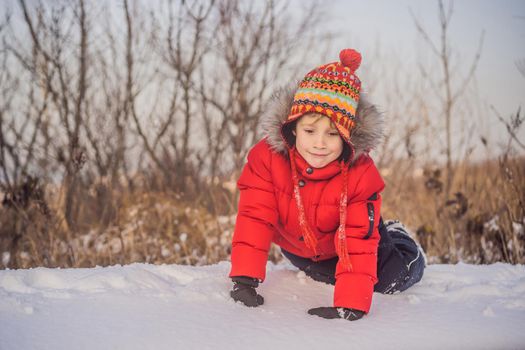 Boy in red fashion clothes playing outdoors. Active leisure with children in winter on cold days. Boy having fun with first snow. Happy little kid is playing in snow, good winter weather.