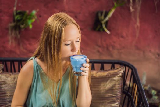 Young woman having a mediterranean breakfast seated at sofa and drinks Trendy drink: Blue latte. Hot butterfly pea latte or blue spirulina latte.