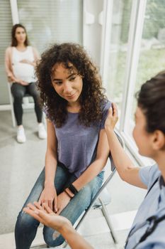 Upset African American teenage girl talks with nurse while waits for gynecologist check up.