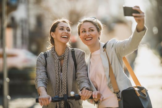 A two successful businesswomen taking a selfie with smartphone while walking through the city.